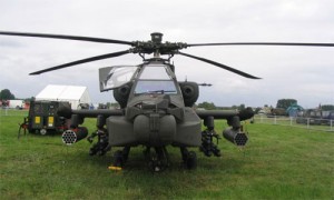 Boeing AH-64 Apache attack helicopter standing in a green field waiting to take off for an operation. It has a four-blade, twin-turbo shaft engines and a nose-mounted sensor . It is armed with a 30 mm (1.18 in) M230 chain gun carried between the main landing gear, under the aircraft's forward fuselage. It has four hardpoints mounted on stub-wing pylons, typically carrying a mixture of AGM-114 Hellfire missiles and Hydra 70 rocket pods.suite for target acquisition and night vision systems.