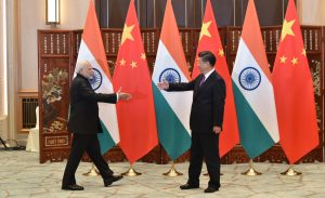 Indian Prime Minister Narendra Modi & Chinese President Xi Jinping walking towards each other with extended hands all set to shake warmly . In the background are the flags of India and China.